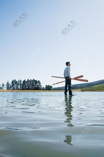 手拿双桨站立在水面上的男人图片