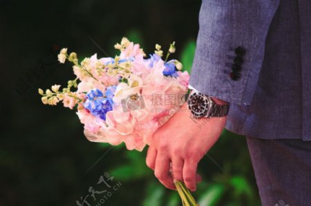 在灰色西装的男人的粉色花束控股和蓝色瓣花
