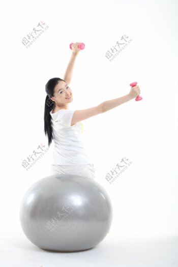 坐在健身球上举哑铃的运动少女图片图片